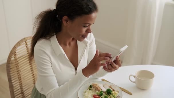 Knappe Afrikaanse Vrouw Kijkt Naar Telefoon Bij Het Ontbijt — Stockvideo
