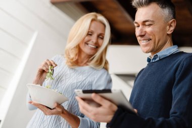 Mutlu orta yaşlı çift evde tabletle web sörfü yapıyor, kahvaltı yapıyor.