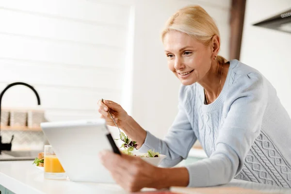Usmívající Blondýnka Středního Věku Drží Tablet Počítač Opírající Kuchyňský Stůl — Stock fotografie