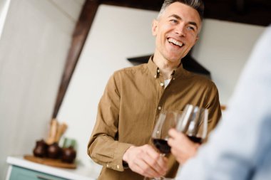 Gülümseyen orta yaşlı çift mutfakta kırmızı şarap içiyor.