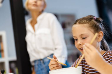 Beyaz anne ve kız mutfakta yemek yiyorlar.