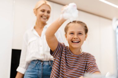 Beyaz anne ve kız evde birlikte bulaşık yıkarken gülümsüyorlar.