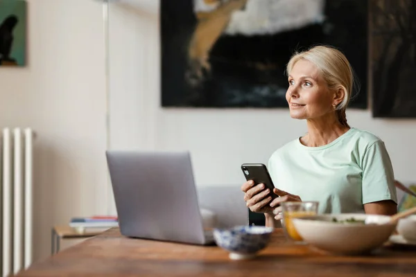 Blond Volwassen Vrouw Met Behulp Van Laptop Mobiele Telefoon Tijdens — Stockfoto