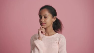 Düşünceli Afrikalı küçük kız pembe stüdyodaki bir şeye katılıyor.