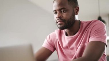 Kanepede dizüstü bilgisayarla konuşan dalgın Afrikalı adam.