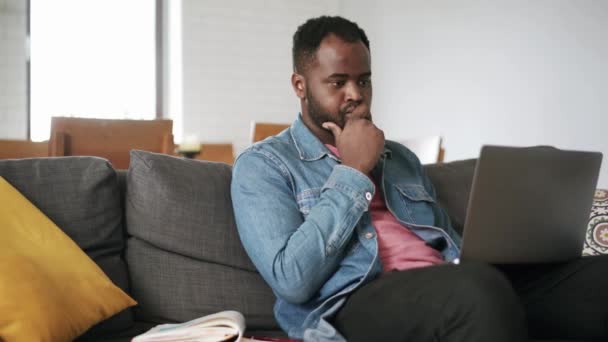 ソファの上の自宅でラップトップで入力する正のアフリカ人男性 — ストック動画