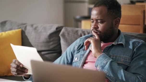 Afrykański Poważny Człowiek Wpisując Coś Notatnika Laptopa Domu Kanapie — Wideo stockowe