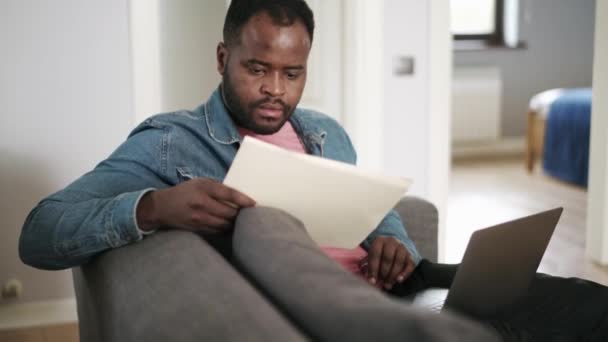 Africano Pensativo Hombre Escribiendo Algo Bloc Notas Portátil Casa Sofá — Vídeo de stock