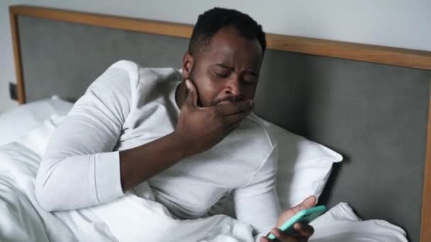 Slaperige Afrikaanse Man Geeuwen Kijken Naar Telefoon Bed — Stockvideo