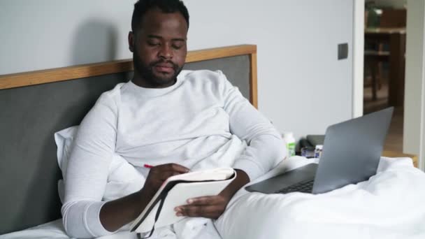Pensiv Afrikansk Man Skriver Något Anteckningsblock Sängen — Stockvideo