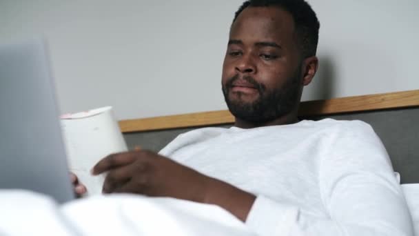 アフリカ人男性がベッドの上でノートパソコンに入力する — ストック動画