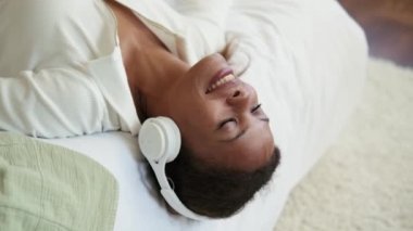 Yatakta kulaklıkla müzik dinleyen gülümseyen Afrikalı kadın.