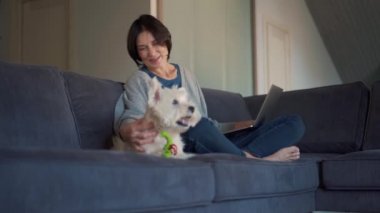 Bilgisayarda çalışan ve köpeğini okşayan mutlu olgun bir kadın.