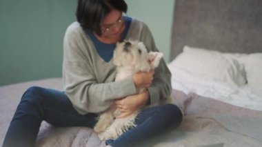 Neşeli olgun bir kadın köpeğini yatakta kucaklıyor.