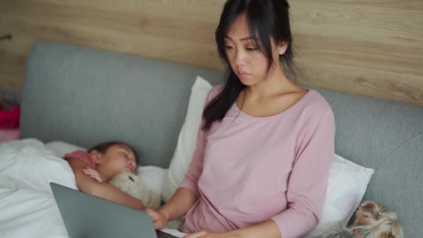 Sério Asiático Mãe Trabalhando Laptop Enquanto Sua Filha Dormindo Cama — Vídeo de Stock