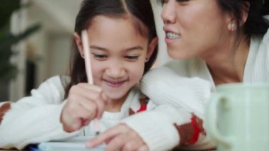 Pozitif Asyalı kız not defterine yazıyor ve annesi onu mutfakta öpüyor.