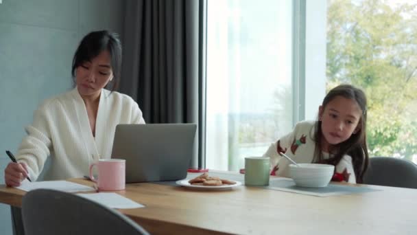 彼女の娘は午前中に何かを求めている間 彼女の娘はノートパソコンで働いているアジアの母親 — ストック動画