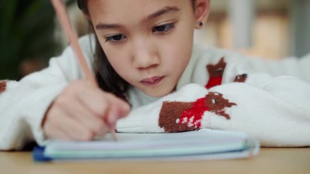 瞑想的なアジアの女の子はノートパッドで書いて 彼女の母親は台所で彼女を撫でて — ストック動画