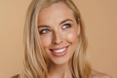 Bej arka planda duran uzun saçlı, mutlu, sarışın bir kadının güzel görüntüsü.