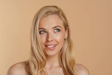 Bej arka planda duran uzun saçlı, mutlu, sarışın bir kadının güzel görüntüsü.