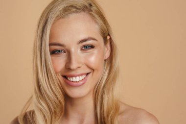 Bej arka planda duran uzun saçlı, mutlu, sarışın bir kadının güzel görüntüsü.