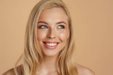 Bej arka planda duran uzun saçlı, mutlu, sarışın bir kadının güzel görüntüsü.