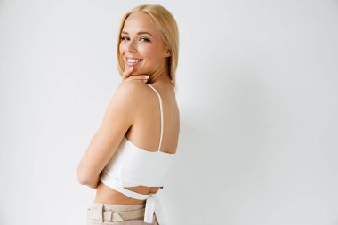 Beyaz arka planda izole edilmiş kameraya bakarken gülümseyen genç sarışın kadın.