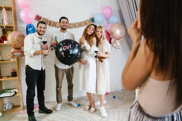 Group of happy friends at a gender reveal baby shower, holding balloon, taking a photo by a photographer