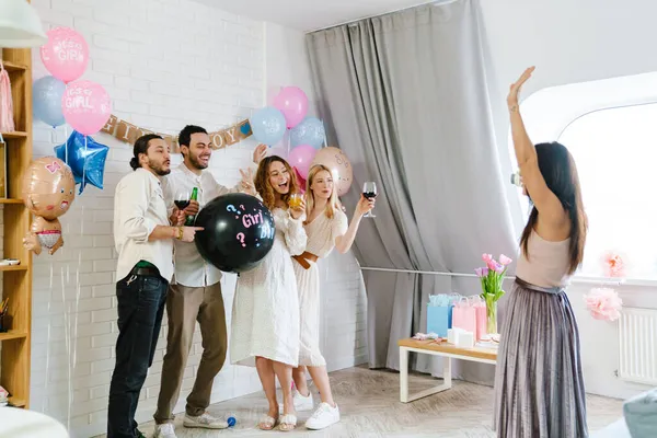 Group of happy friends at a gender reveal baby shower, holding balloon
