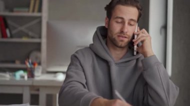 Kapüşonlu adam telefonda konuşuyor ve ofiste gazete okuyor.