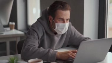 Ofiste dizüstü bilgisayarla çalışan koruyucu maskeli kendine güvenen bir adam.