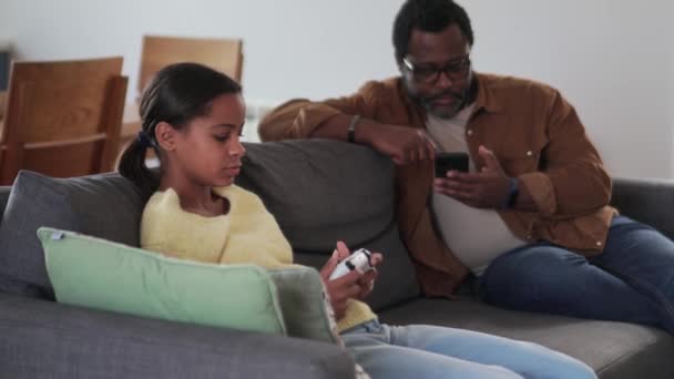 父親が家で誰かに電話してる間にアフリカ人の女の子がコンソールで遊んでた — ストック動画