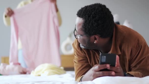 Padre Africano Mirando Teléfono Mientras Hija Dobla Sus Cosas Casa — Vídeo de stock