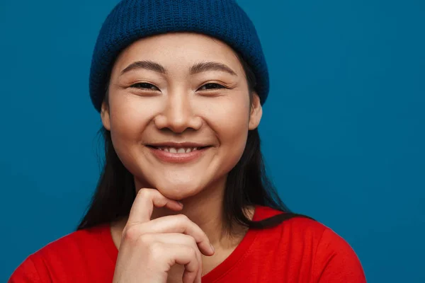 一个快乐而随意的年轻亚洲女人头戴帽子站在蓝色墙的背景下看着相机的画像 — 图库照片
