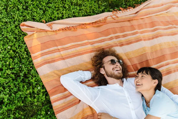 Счастливая Улыбающаяся Молодая Многонациональная Пара Лежащая Одеяле Зеленой Траве Парке — стоковое фото