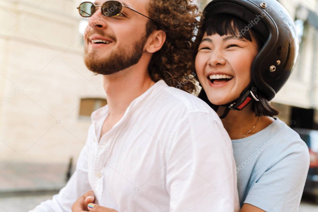 Happy young multiethnic couple on scooter enjoying ride on a street close up