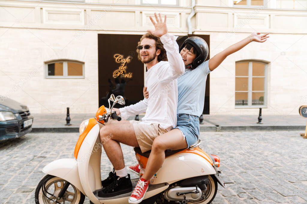 Happy young multiethnic couple on scooter enjoying ride on a street