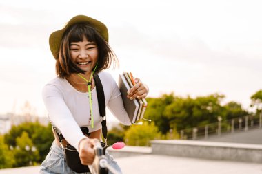 Şapkalı genç Asyalı kadın köpeğiyle dışarıda yürürken gülümsüyor.