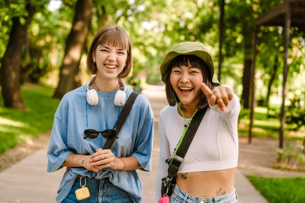 Δύο Πολυφυλετικές Γυναίκες Δείχνουν Την Κάμερα Και Γελούν Ενώ Περπατούν — Φωτογραφία Αρχείου