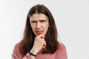 Beyaz arka planda el ele tutuşarak duran, uzun kahverengi saçlı, dalgın beyaz bir adamın portresi.