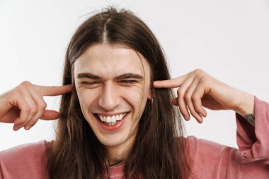 Beyaz duvarın arkasında duran, kulakları tıkayan, uzun kahverengi saçlı, mutlu beyaz bir adamın portresi.