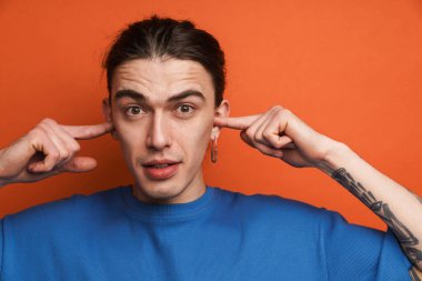 Beyaz duvarın arkasında dikilen, kulakları tıkayan sıradan bir gencin portresi.