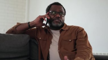 Gülümseyen Afrikalı adam evde telefonla konuşuyor.