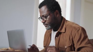 Dizüstü bilgisayarda çalışan ve mutfakta çay içen konsantre bir adam.