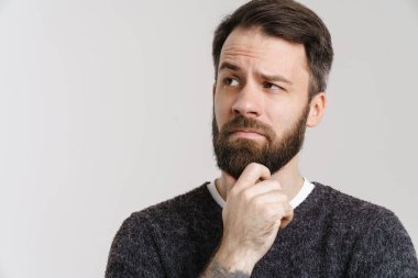 Beyaz şaşkın sakallı beyaz adam beyaz arka planda yalnız başına poz veriyor ve bakıyor.