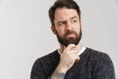 Beyaz şaşkın sakallı beyaz adam beyaz arka planda yalnız başına poz veriyor ve bakıyor.