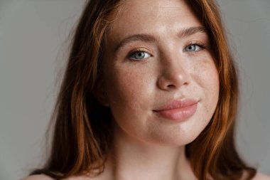 Duvarın arkasında duran uzun kızıl saçlı, gülümseyen, kıvrımlı genç bir kadının portresi.