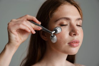 Genç, sakin, beyaz bir kadın. Masaj yapıyor. Gri arka planda yuvarlanıyor.