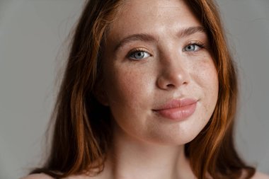 Duvarın arkasında duran uzun kızıl saçlı, gülümseyen, kıvrımlı genç bir kadının portresi.