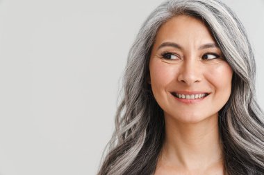 Tişörtsüz, beyaz saçlı, gülümseyen ve beyaz arka planda izole edilmiş bir tarafa bakan olgun bir kadın.